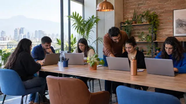 Mesa de taller con personas trabajando en notebooks y un facilitador ayudando
